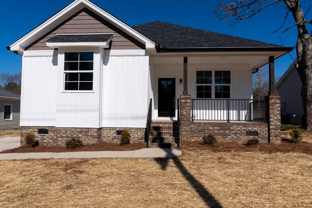 Modern white house with brick accents and a porch under clear blue sky. New construction.