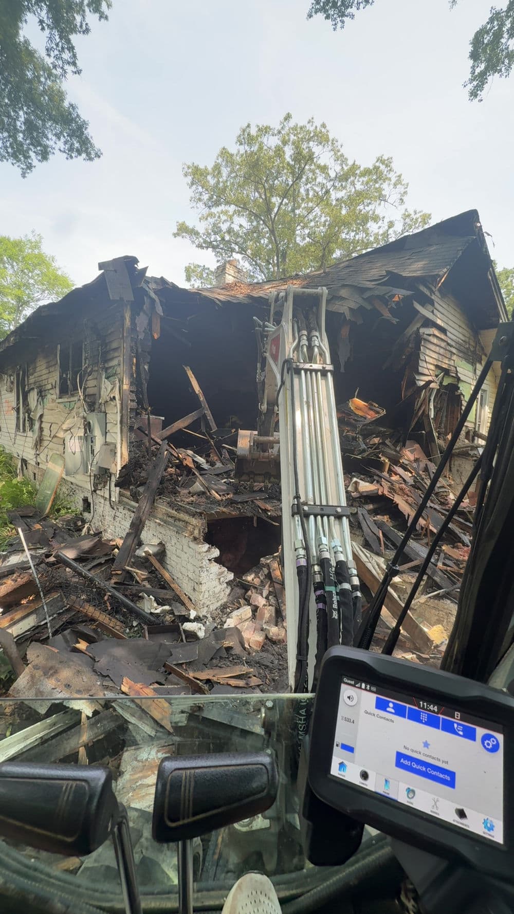 Burnt house with collapsed structure viewed from construction equipment, showcasing fire damage.