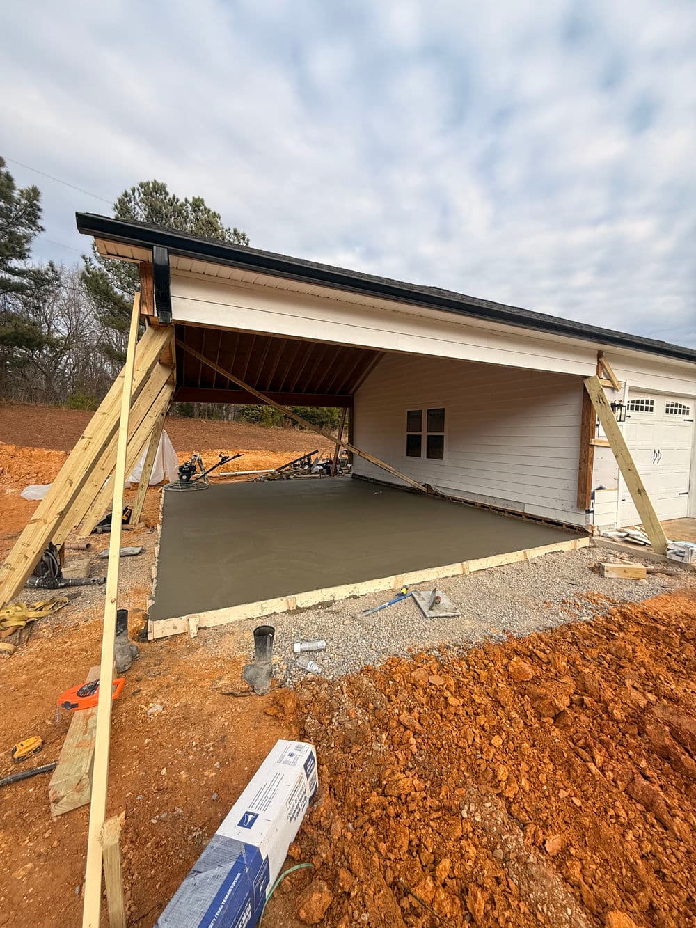 Construction site of a house with freshly poured concrete slab and wooden supports.