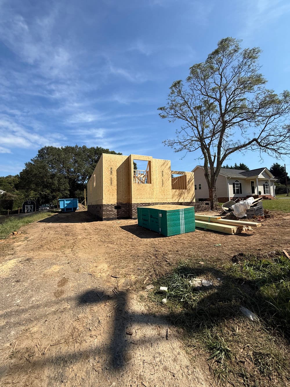 Newly constructed house framing with materials on site under blue sky.