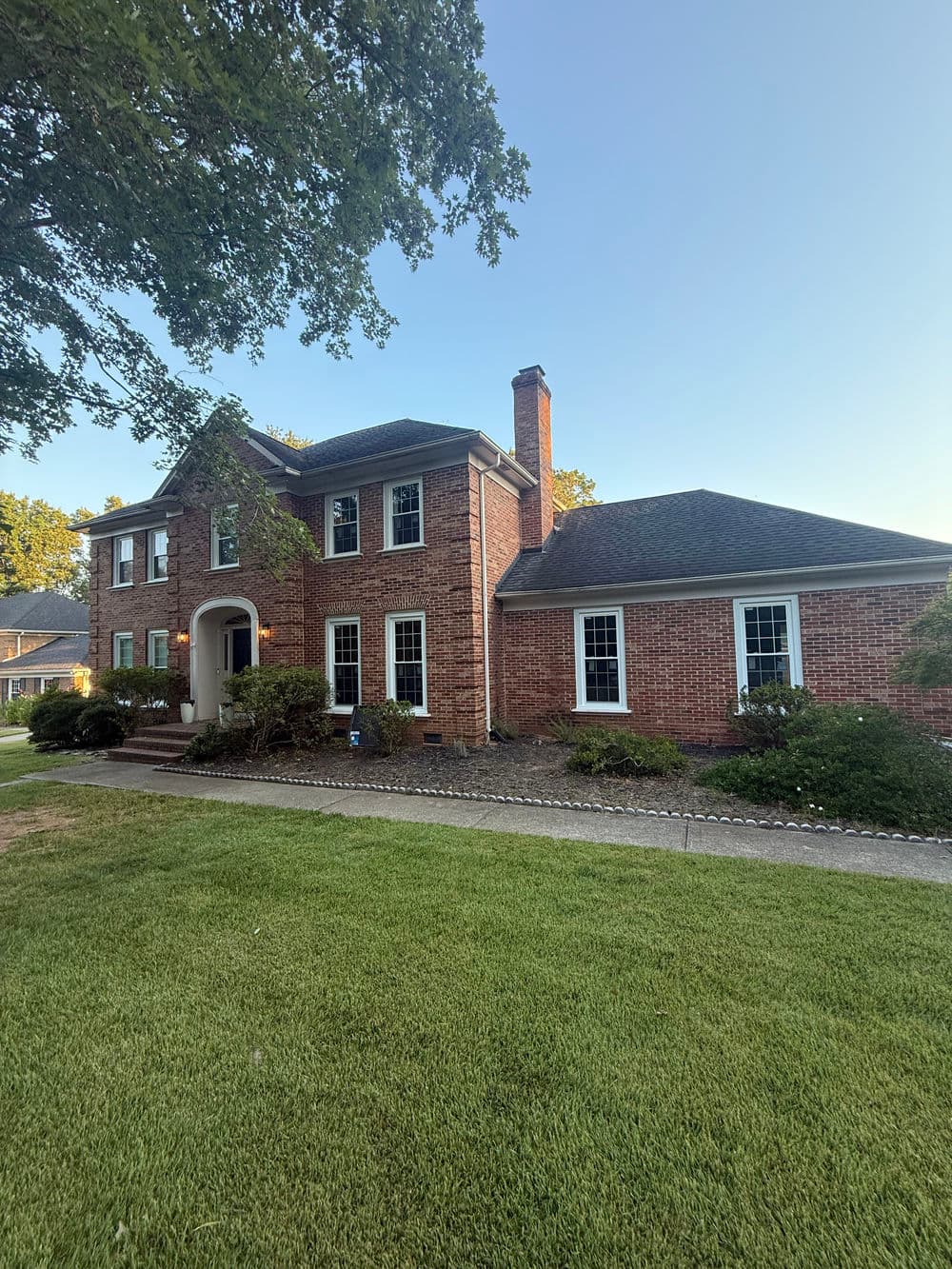 Two-story brick house with a landscaped yard and clear blue sky background.