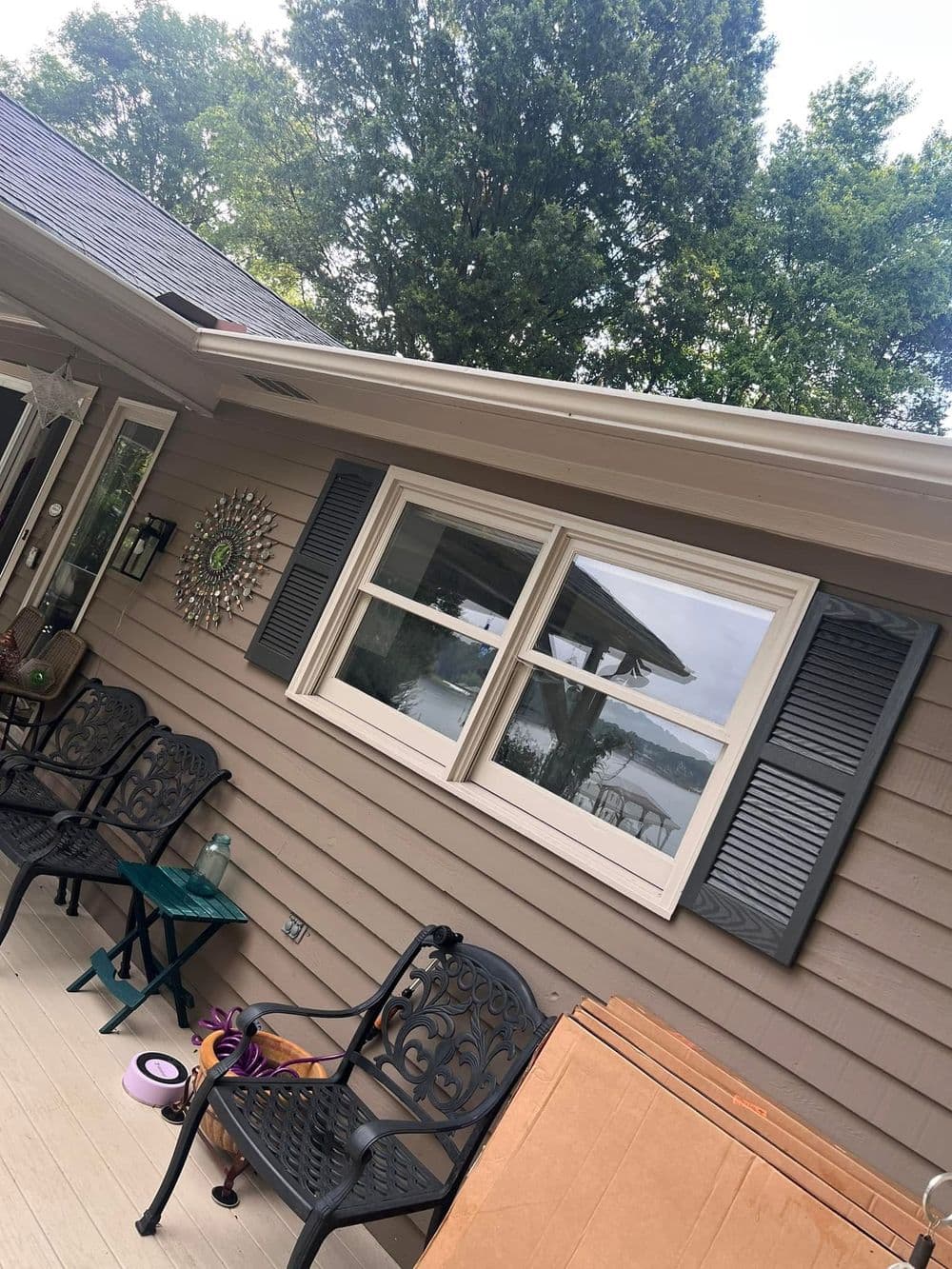 Cozy porch with black chairs, window, and view of trees and lake in the background.