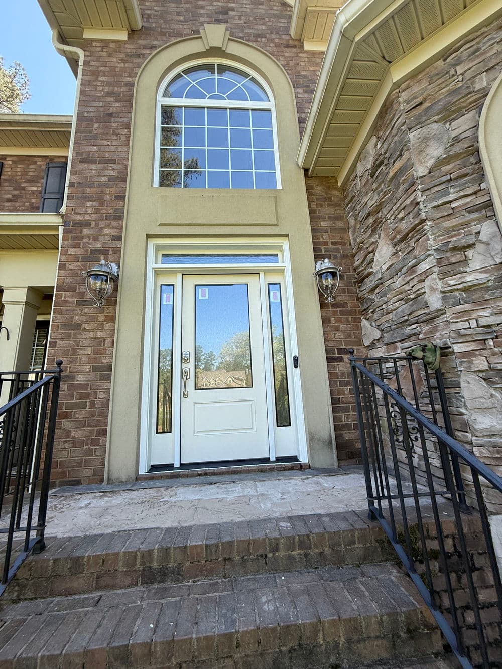 Grand entrance of a brick home with arched windows and stone accents, featuring a white door.
