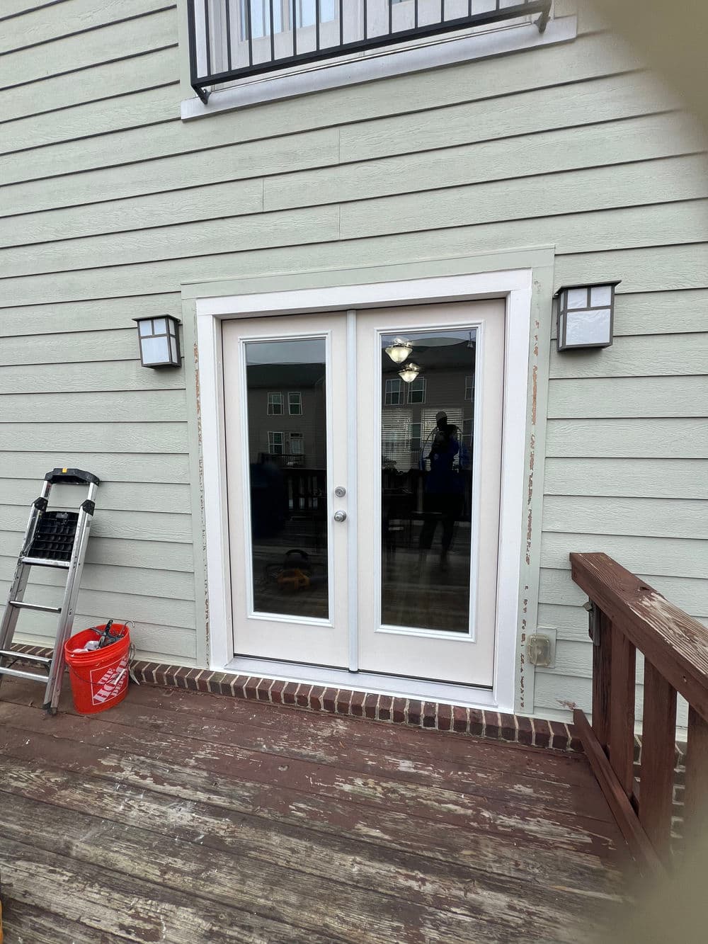 Double glass patio doors leading to a wooden deck, with a ladder and bucket nearby.
