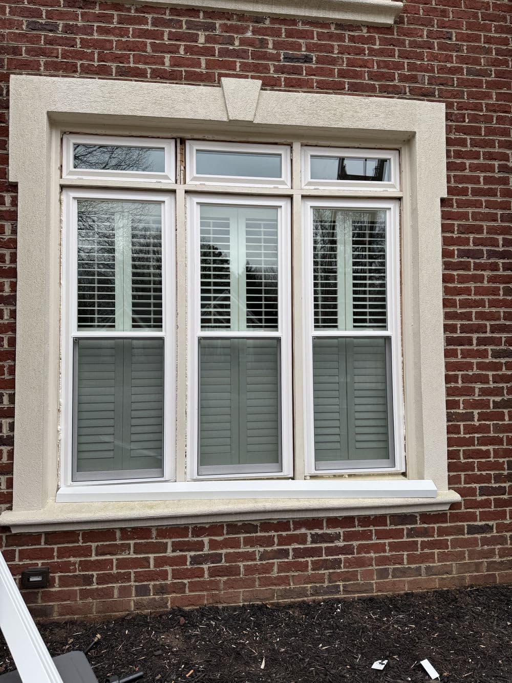 Three-pane window with white shutters on a brick house exterior.