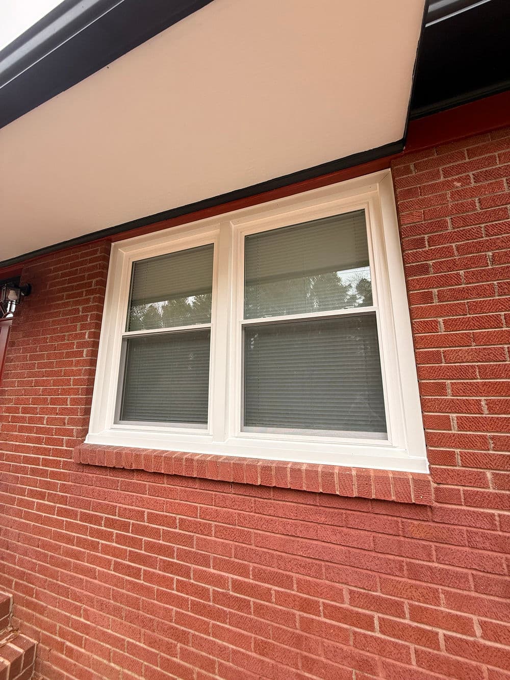 Two white-framed windows on a red brick wall, featuring blinds for privacy.