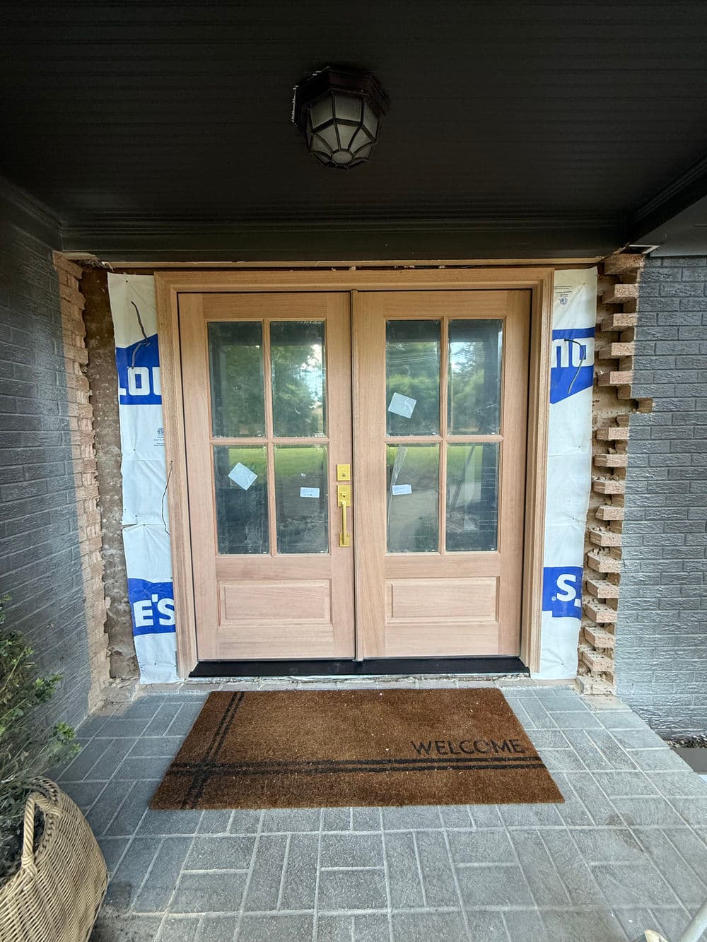 Newly installed double front doors with a welcome mat on a house under renovation.