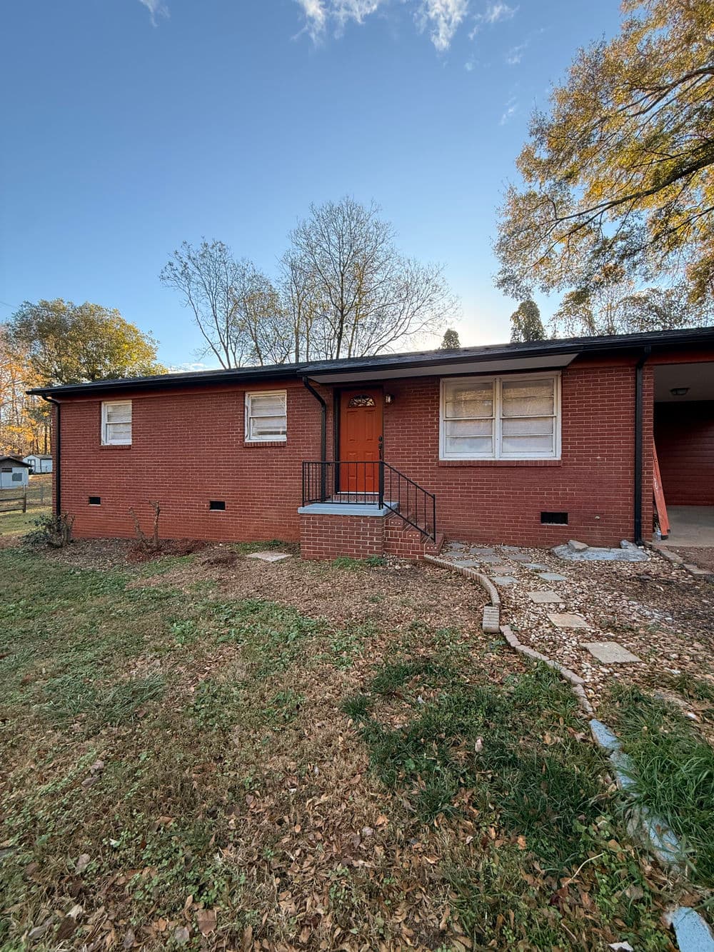 Brick house with orange door, landscaped yard, and clear blue sky in the background.