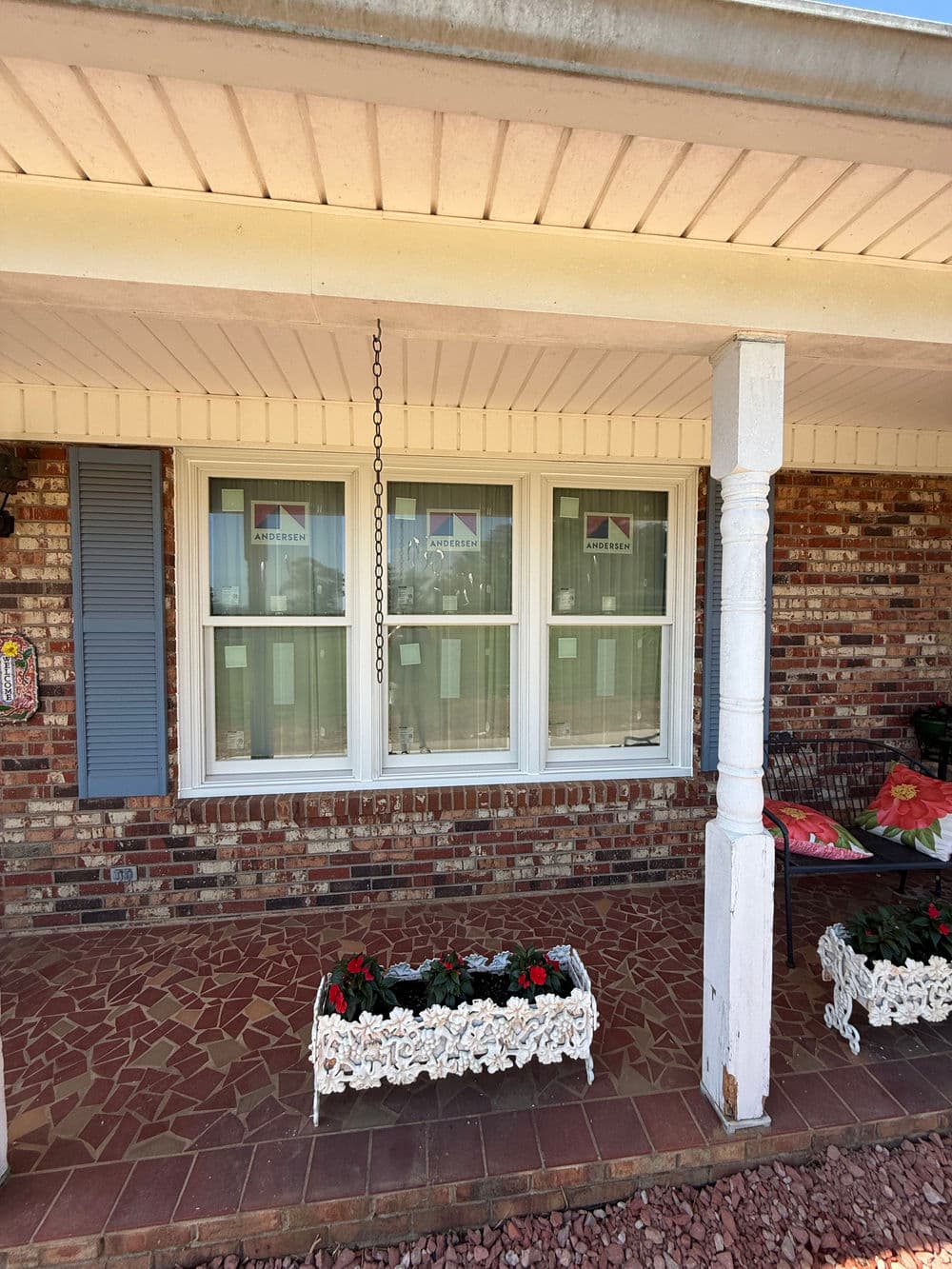 Front porch of a brick house featuring white window trim and flower planters with red flowers.