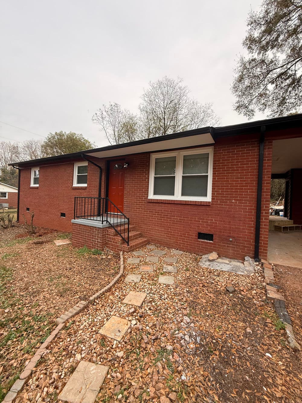 Red brick house with a welcoming front porch and steps, surrounded by natural landscaping.