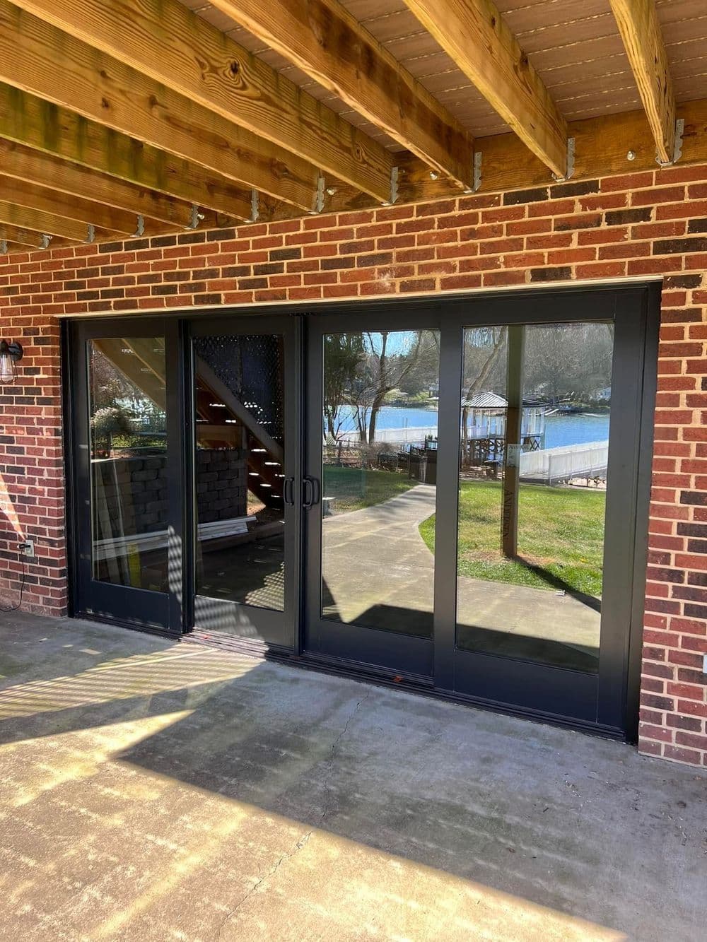 Modern black sliding glass doors opening to a scenic lakeside view, under a wooden deck.