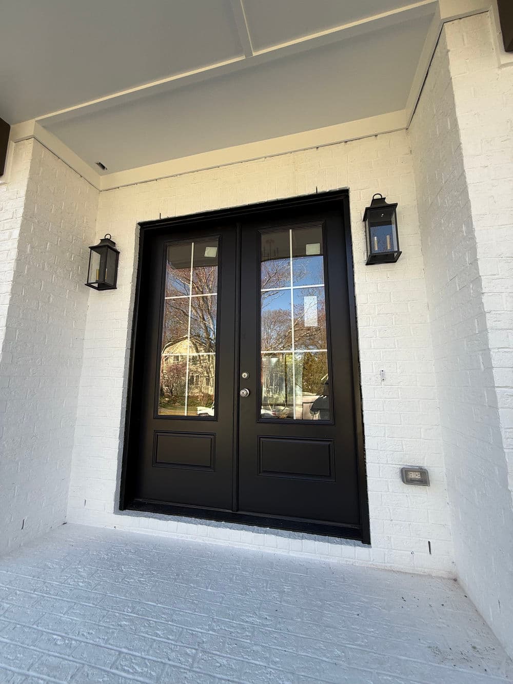 Elegant black double doors with glass inserts, framed by white brick wall and lanterns.