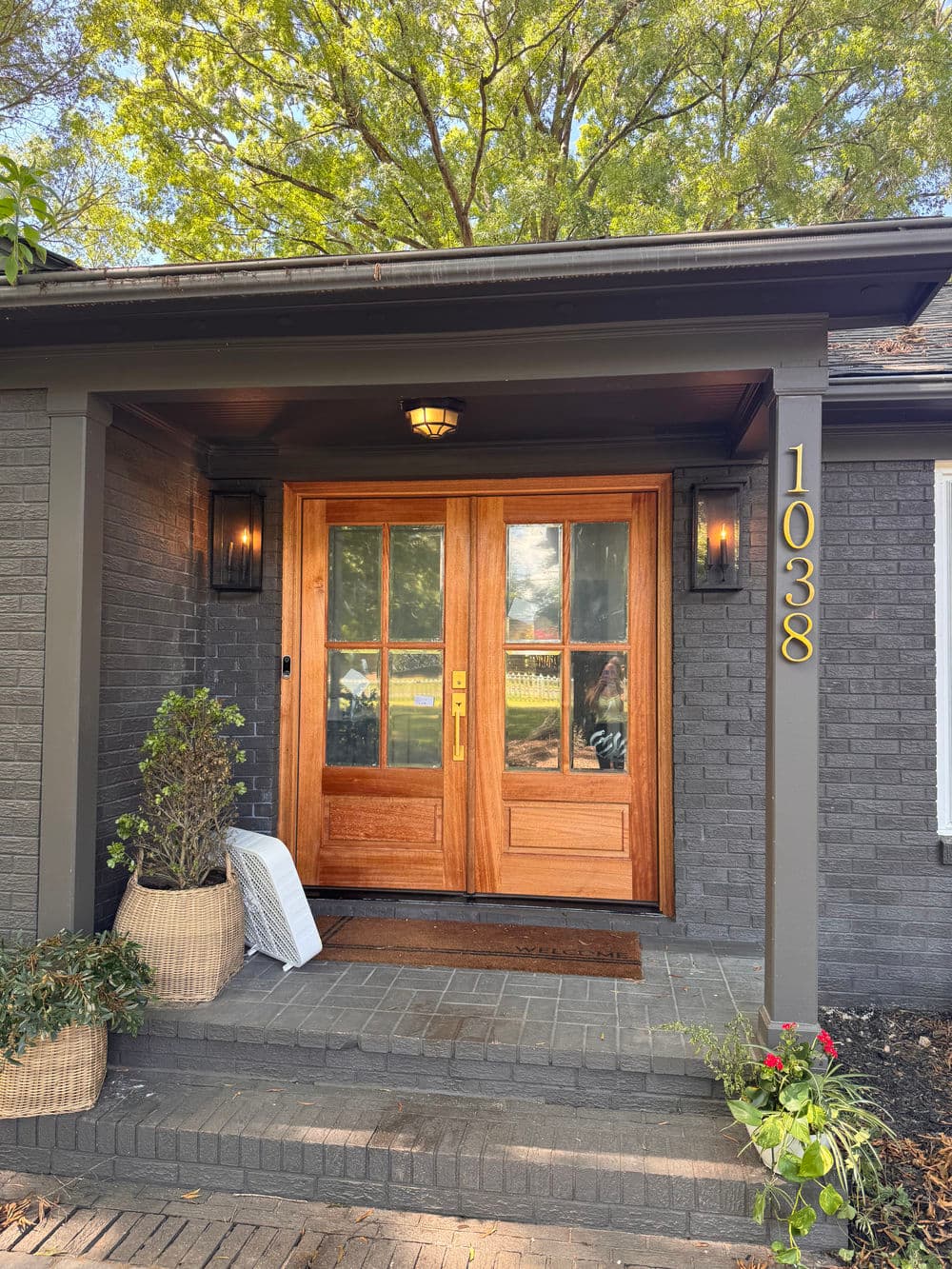 Charming entrance with wooden double doors, house number 1038, and landscaped porch.